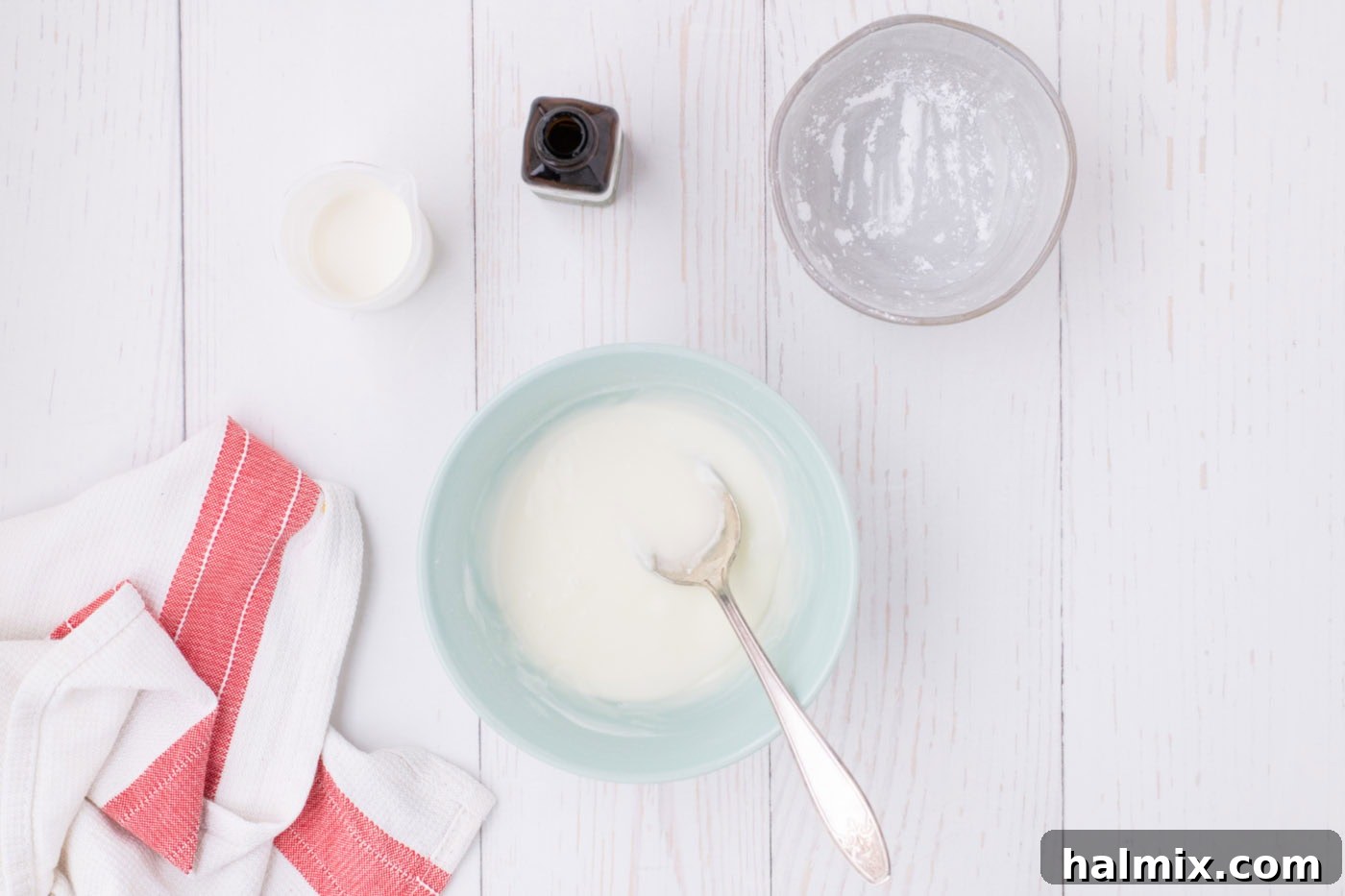 A small glass bowl containing a smooth, white powdered sugar glaze with a spoon resting in it, ready to be applied to the baked pie.