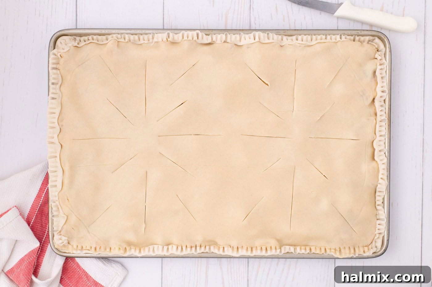 Close-up of the top crust of an unbaked apple slab pie with several evenly spaced slits cut into it for steam release during baking.