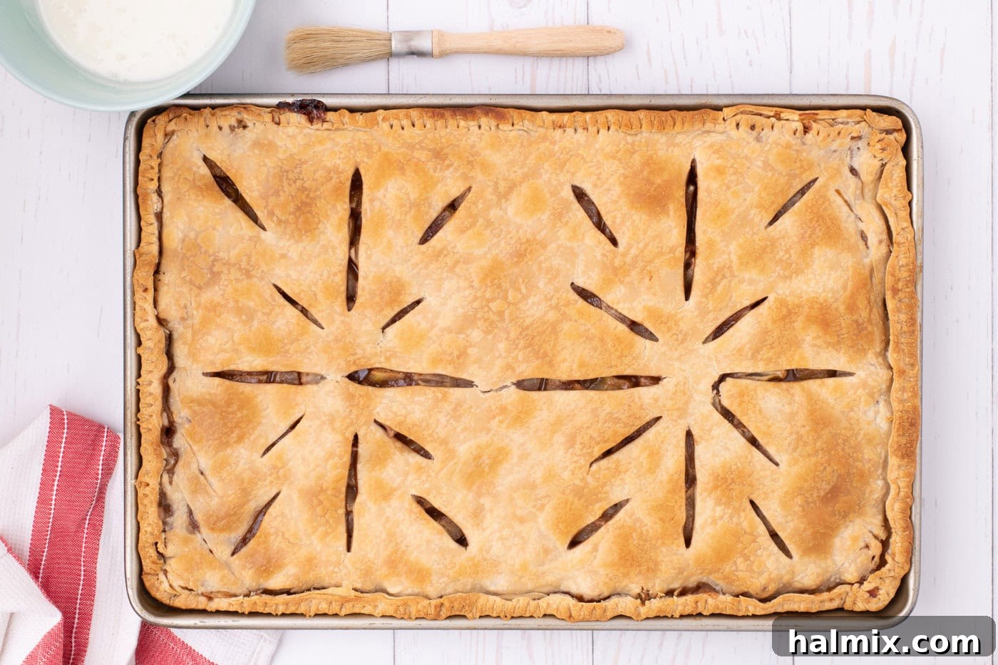 A freshly baked apple slab pie, golden brown and still in its jelly roll pan, cooling on a wire rack.