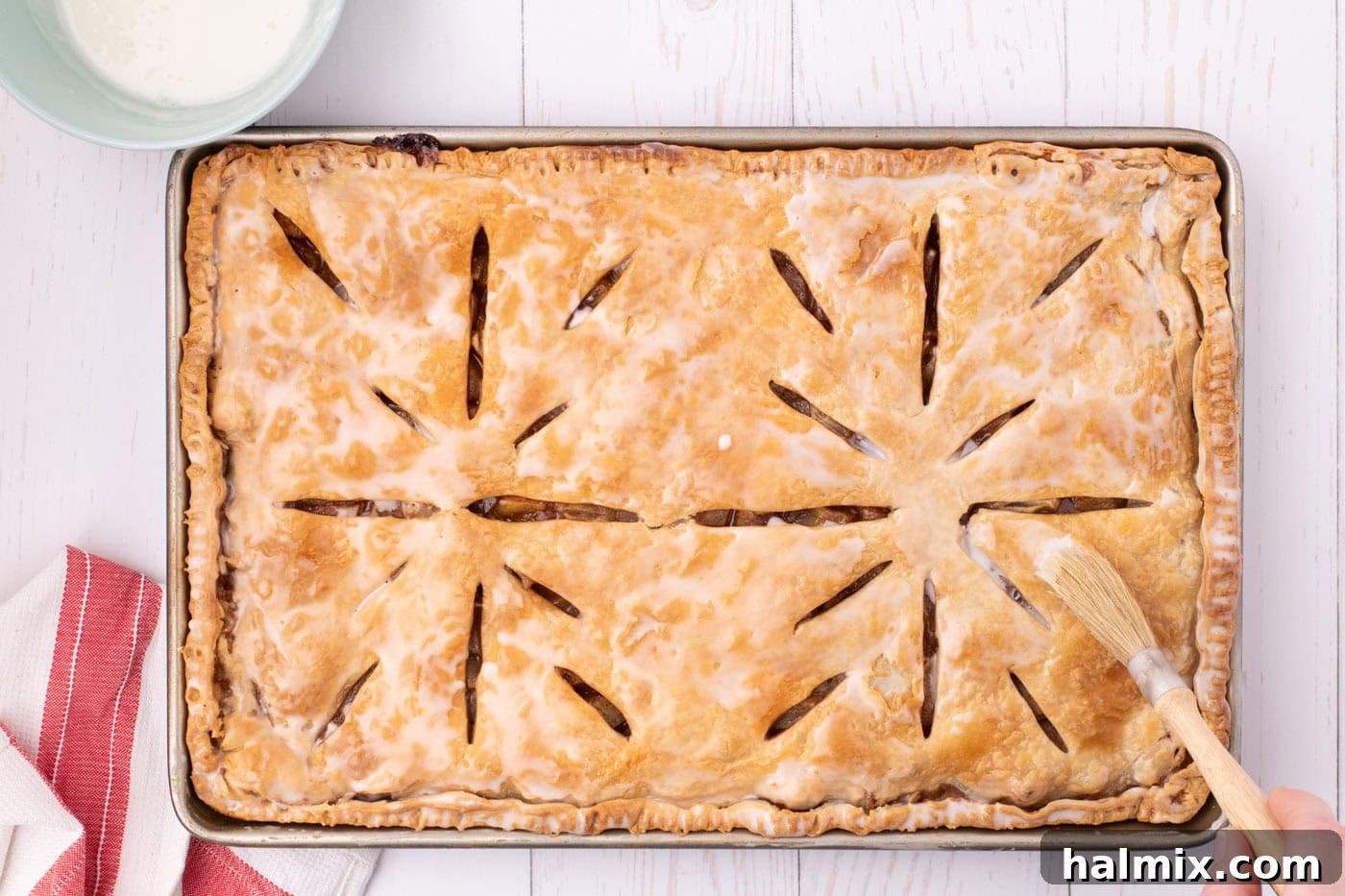 A baked apple slab pie in a jelly roll pan, beautifully coated with a smooth, white powdered sugar glaze, ready for final setting.