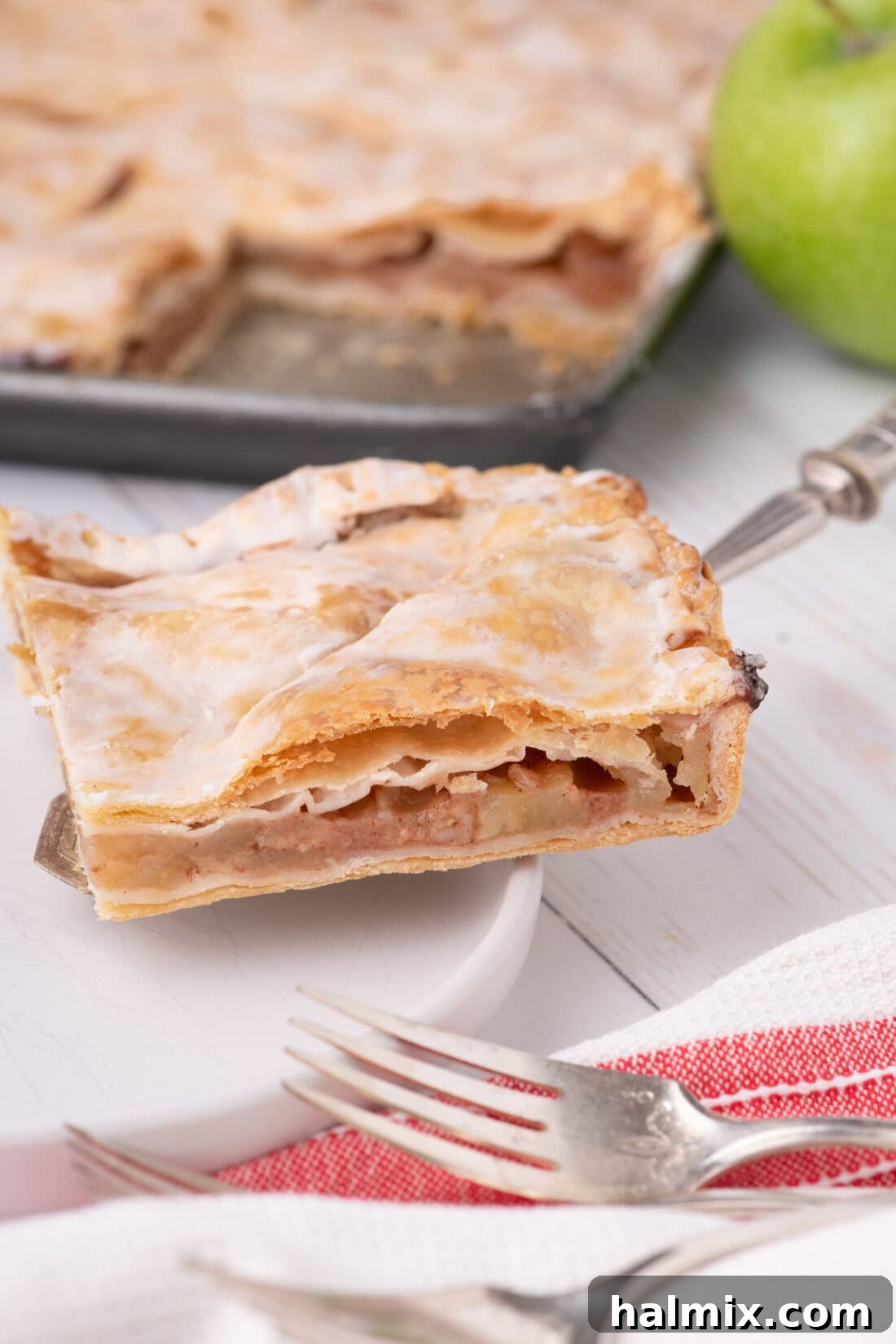 A perfectly golden slice of Apple Slab Pie, featuring a rich apple filling and a delicate flaky crust, served on a white plate ready to be enjoyed.