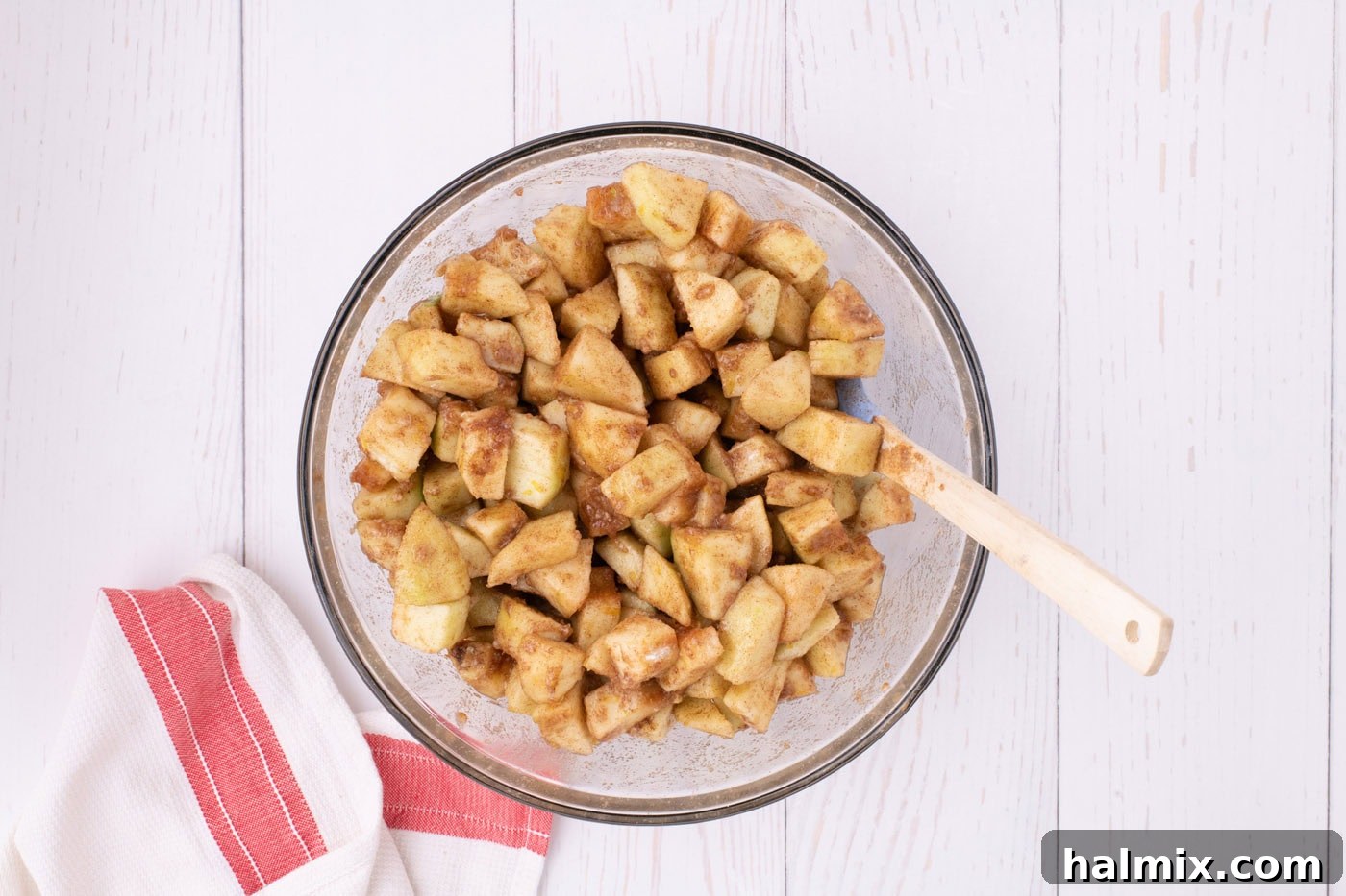 Chopped Granny Smith apples generously coated in a cinnamon, nutmeg, sugar, and flour mixture, ready for the pie filling, in a large glass bowl.