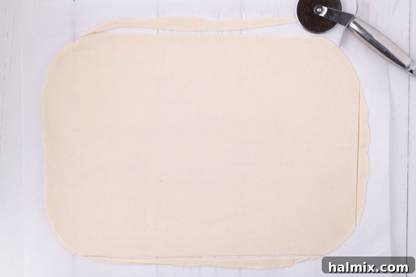 Two pie dough circles rolled out and joined together into a large rectangle, sized for a jelly roll pan, on a parchment-lined surface.
