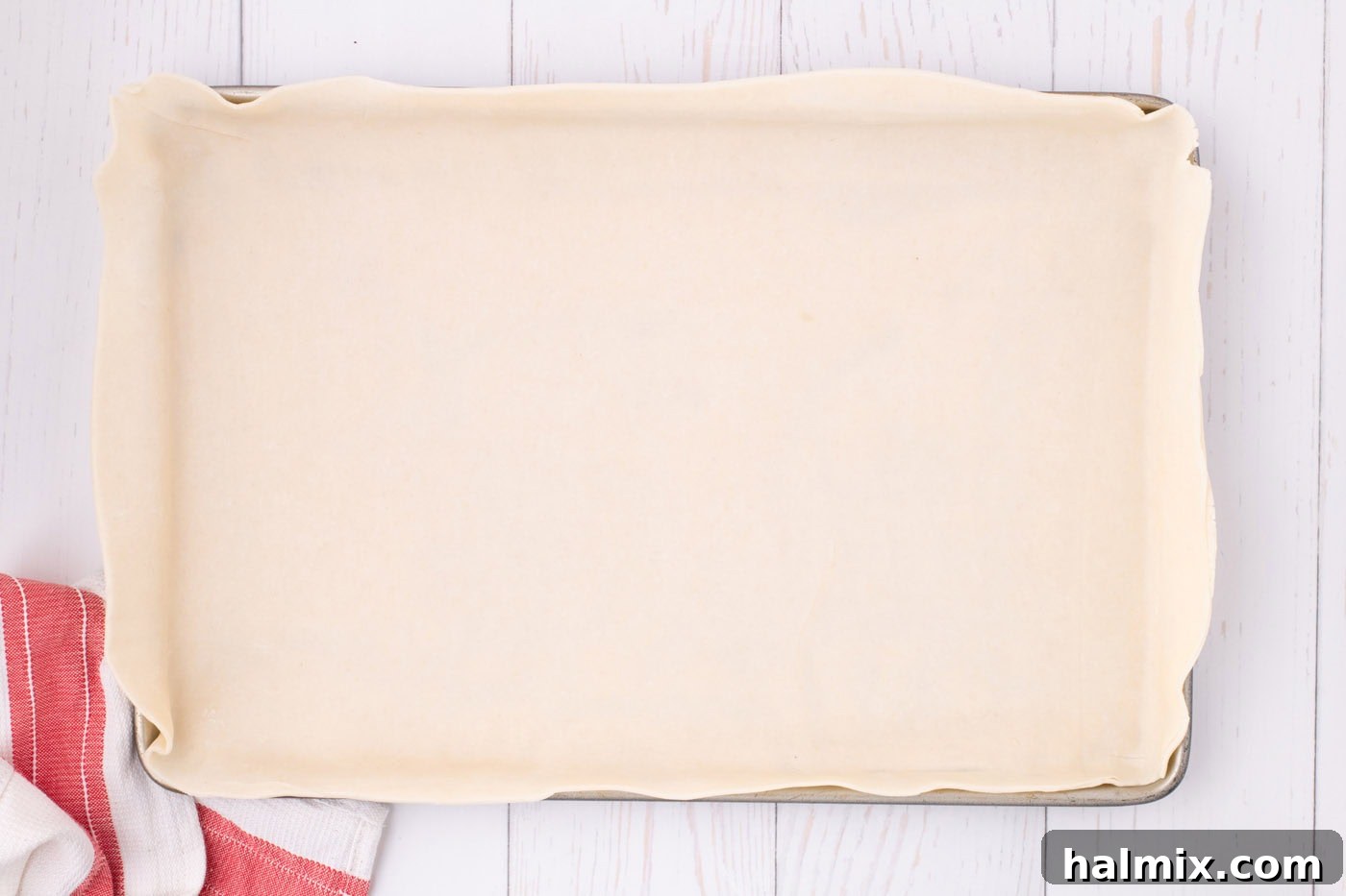 A large rectangular pie dough carefully laid into a jelly roll pan, forming the bottom crust for the apple slab pie, with edges slightly overhanging.