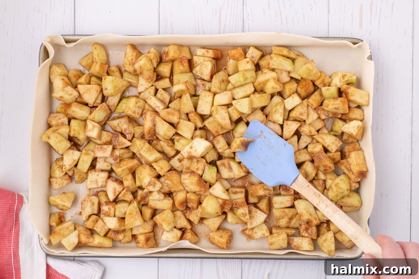 Chopped apple filling, richly spiced and ready for baking, spread evenly over the pie dough base in a sheet pan.