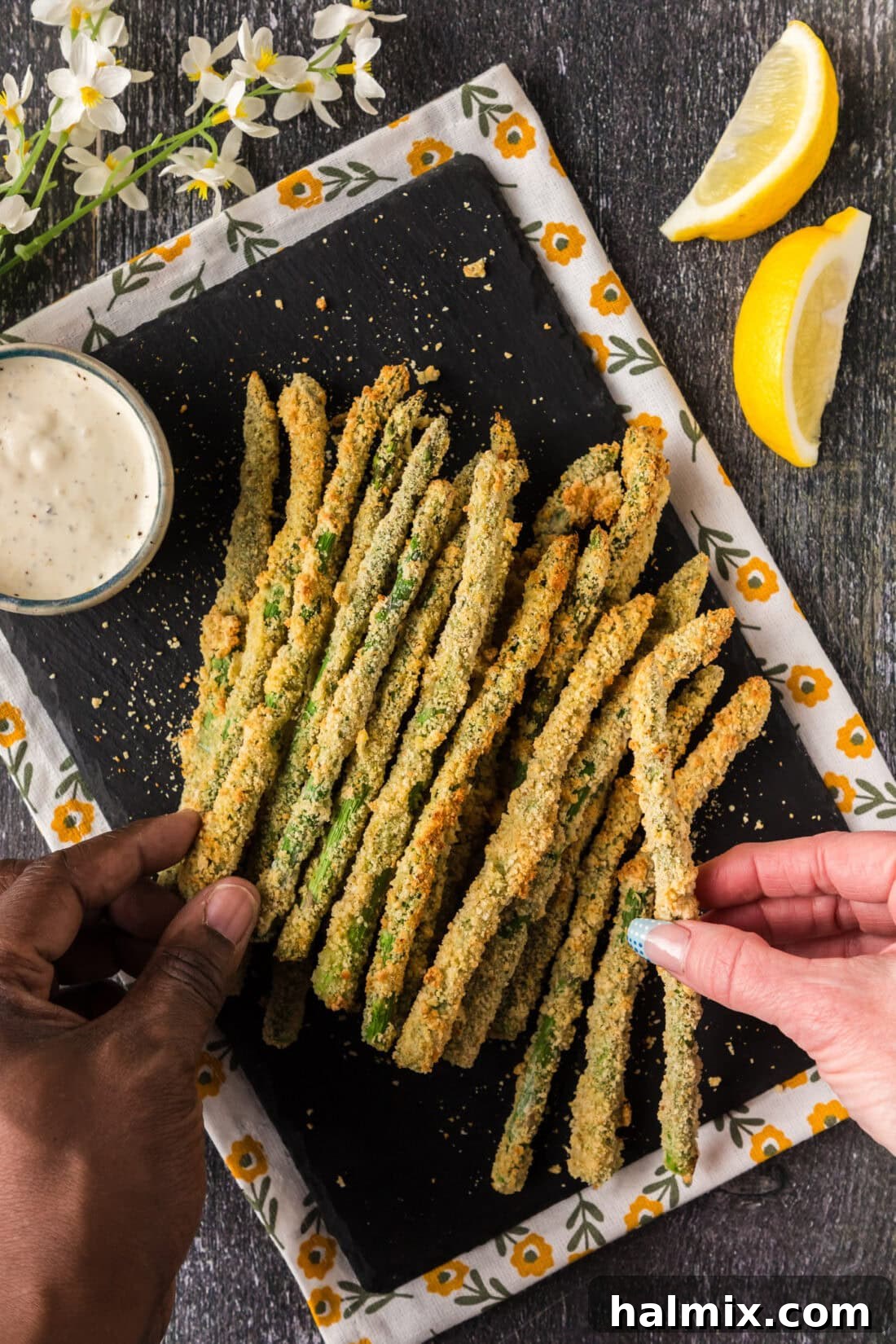 Crispy Air Fryer Asparagus 2 Two hands each picking up an Air Fryer Fried Asparagus spear from a platter