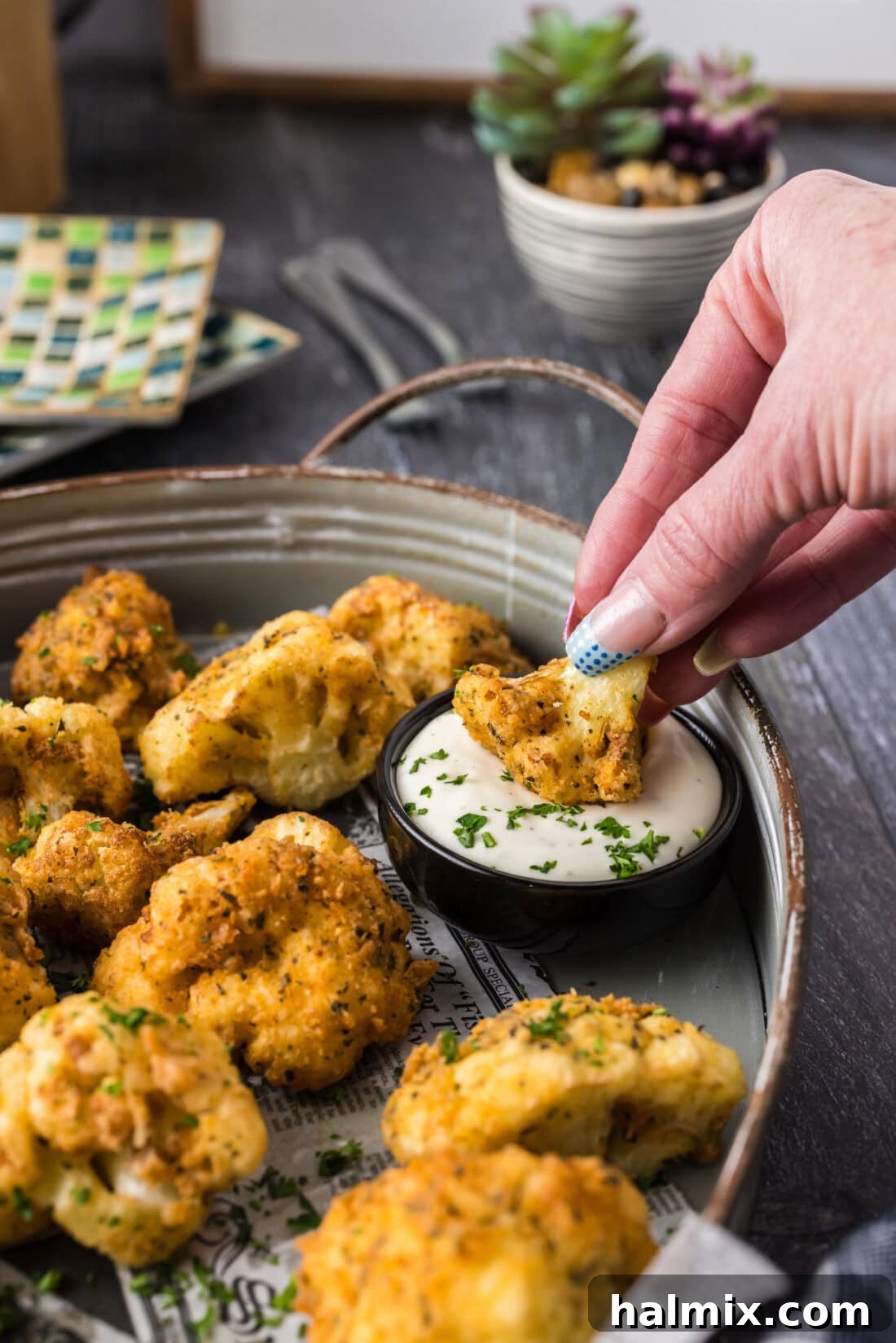 Crispy Golden Cauliflower 3 A hand dipping a perfectly golden fried cauliflower floret into a bowl of creamy ranch dressing