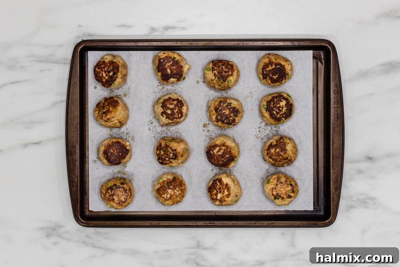 browned chicken meatballs on a parchment lined baking sheet