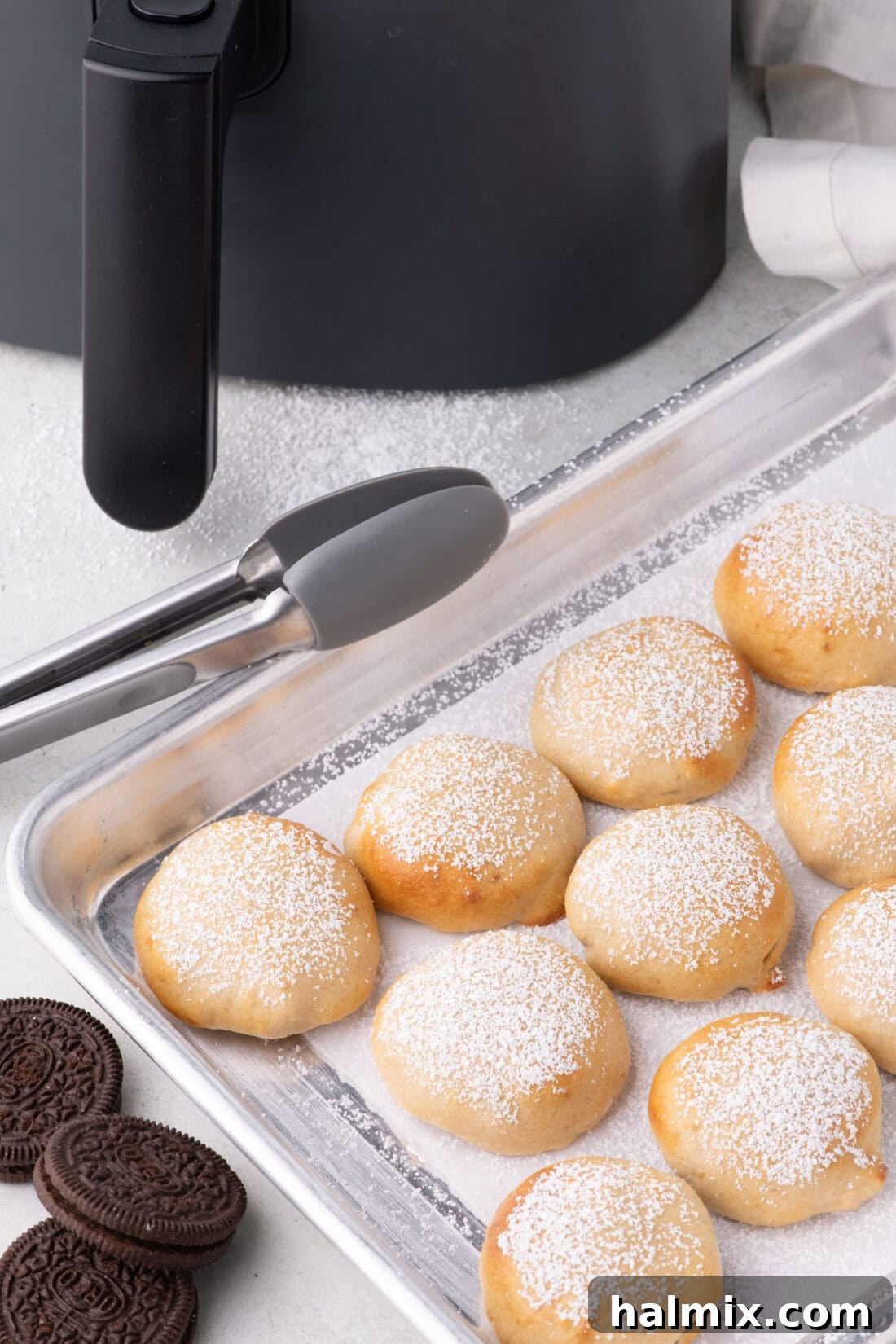 Air Fryer Oreo Magic 10 Air Fryer Oreos arranged on a parchment lined baking sheet, with several already dusted with powdered sugar