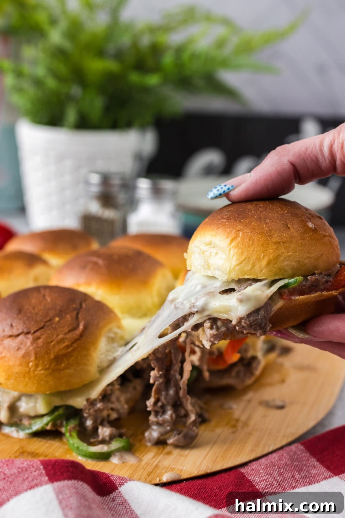 Philly Cheesesteak Slider Delights 2 Hand pulling up a cheesy Philly Cheesesteak Slider from the board of Philly Cheesesteak Sliders