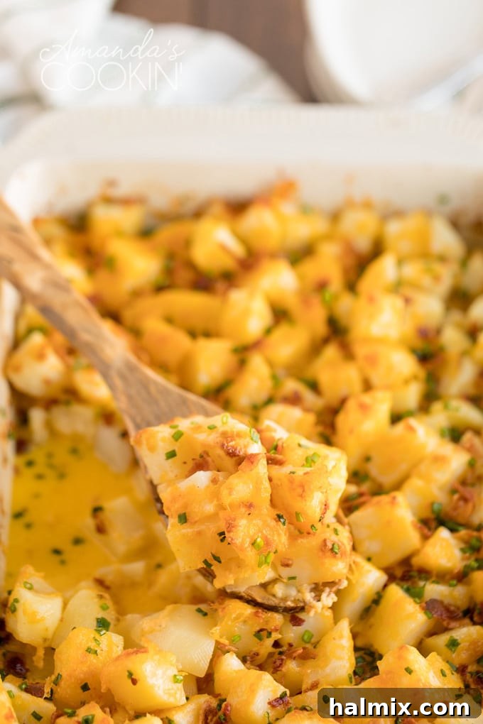 A wooden spoon scoops a generous portion of creamy, cheesy potatoes from a large casserole dish, highlighting the rich texture and melted cheese.
