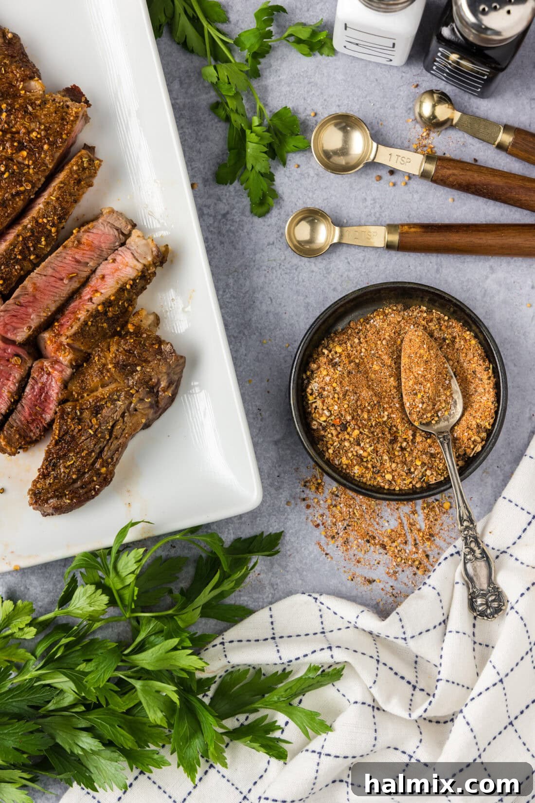 Bowl of Homemade Montreal Steak Seasoning with a spoon in it and cooked steak to the side
