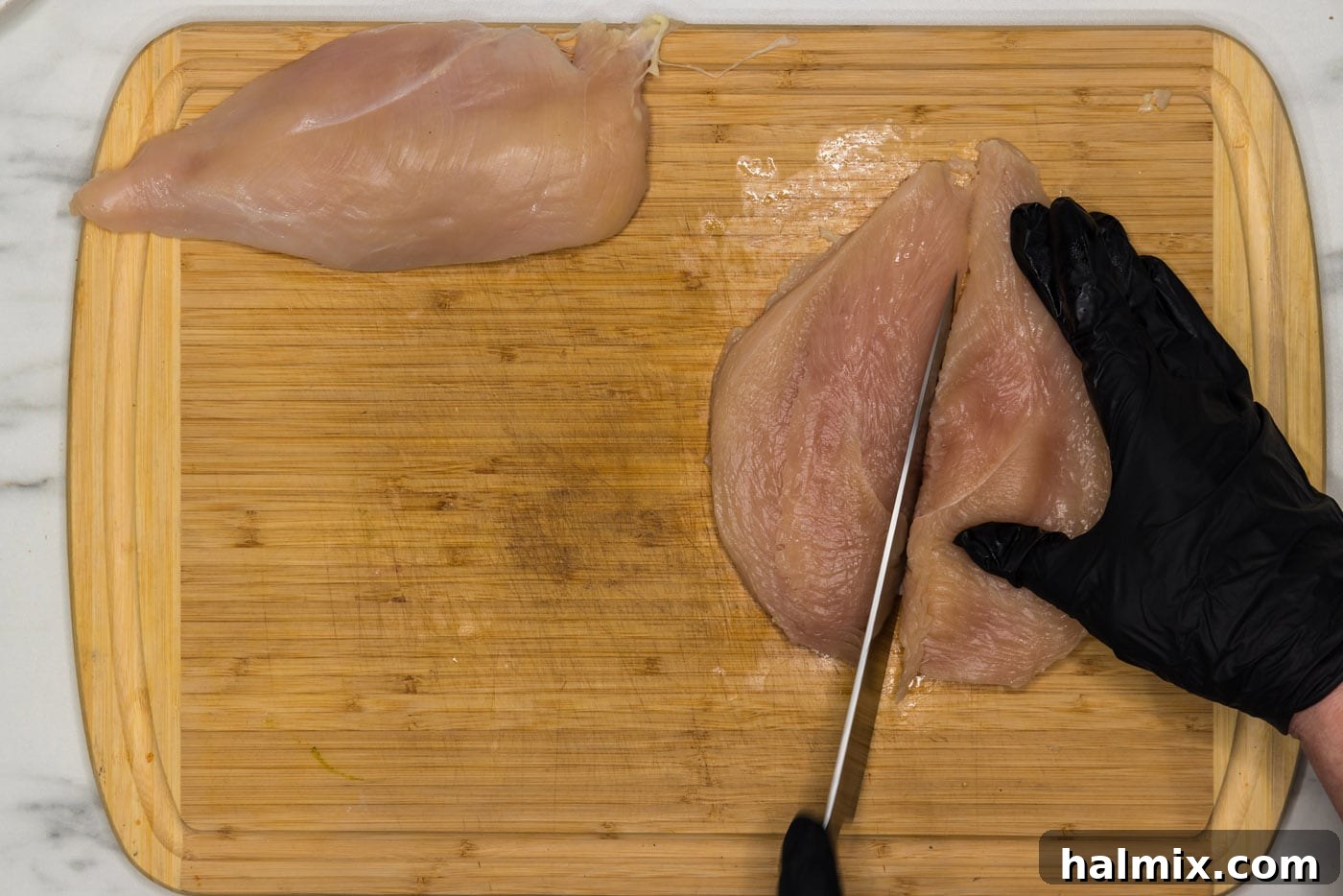 Slicing a chicken breast in half lengthwise with a knife.