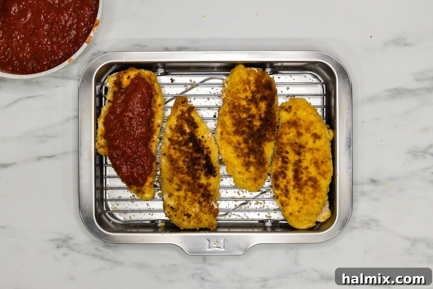 Fried chicken cutlets in a baking pan, topped with marinara sauce.