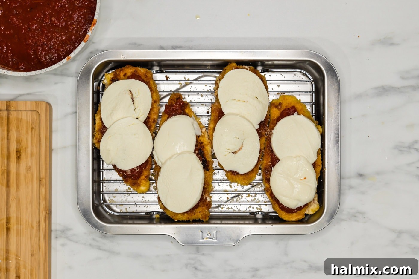 Sliced mozzarella cheese placed on top of marinara-coated chicken cutlets.