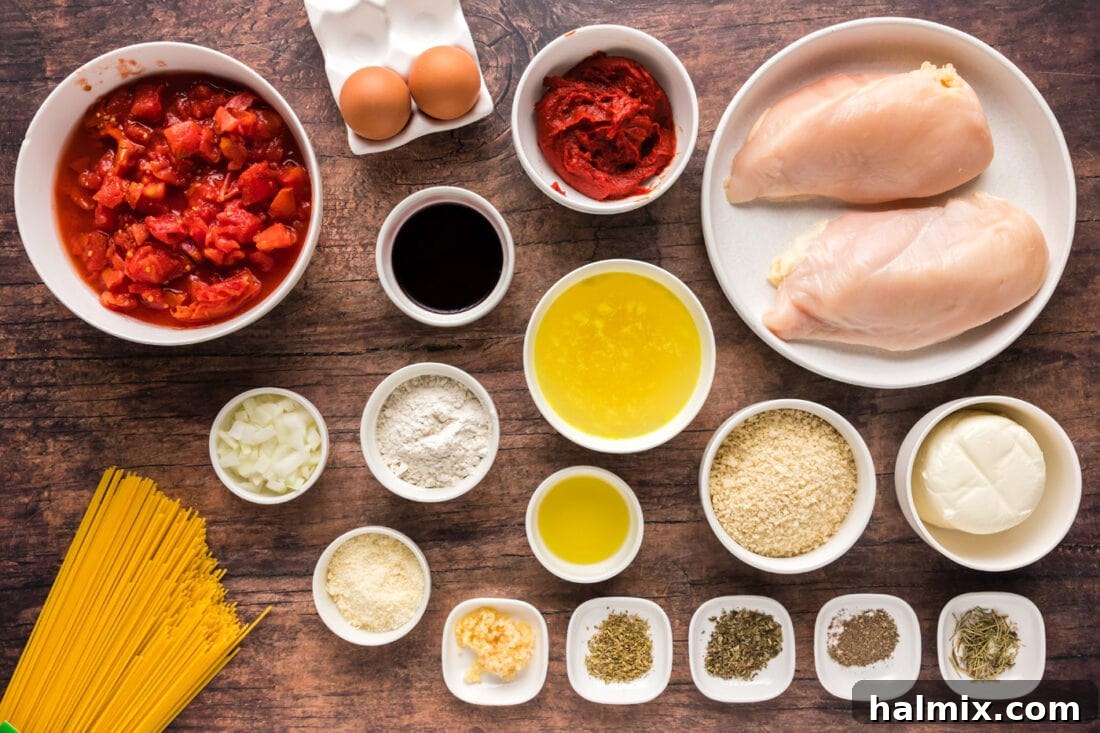 Various fresh ingredients laid out on a wooden board, including tomatoes, herbs, garlic, onion, chicken breasts, and cheese, ready for Chicken Parmesan preparation.
