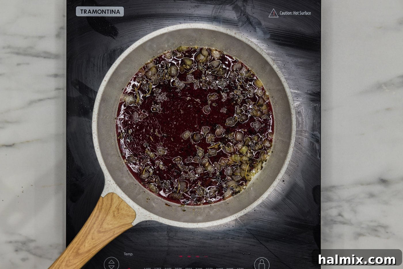 Red wine being added to the skillet with onion and seasonings, beginning to boil.