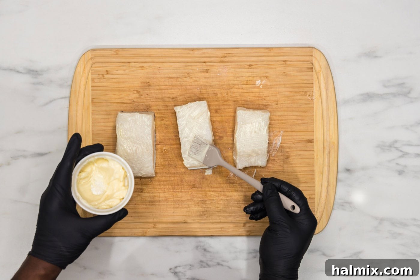 brushing Chilean sea bass with softened butter on a cutting board