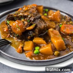 Slow Cooker Oxtail on a grey plate with a sprig of rosemary.