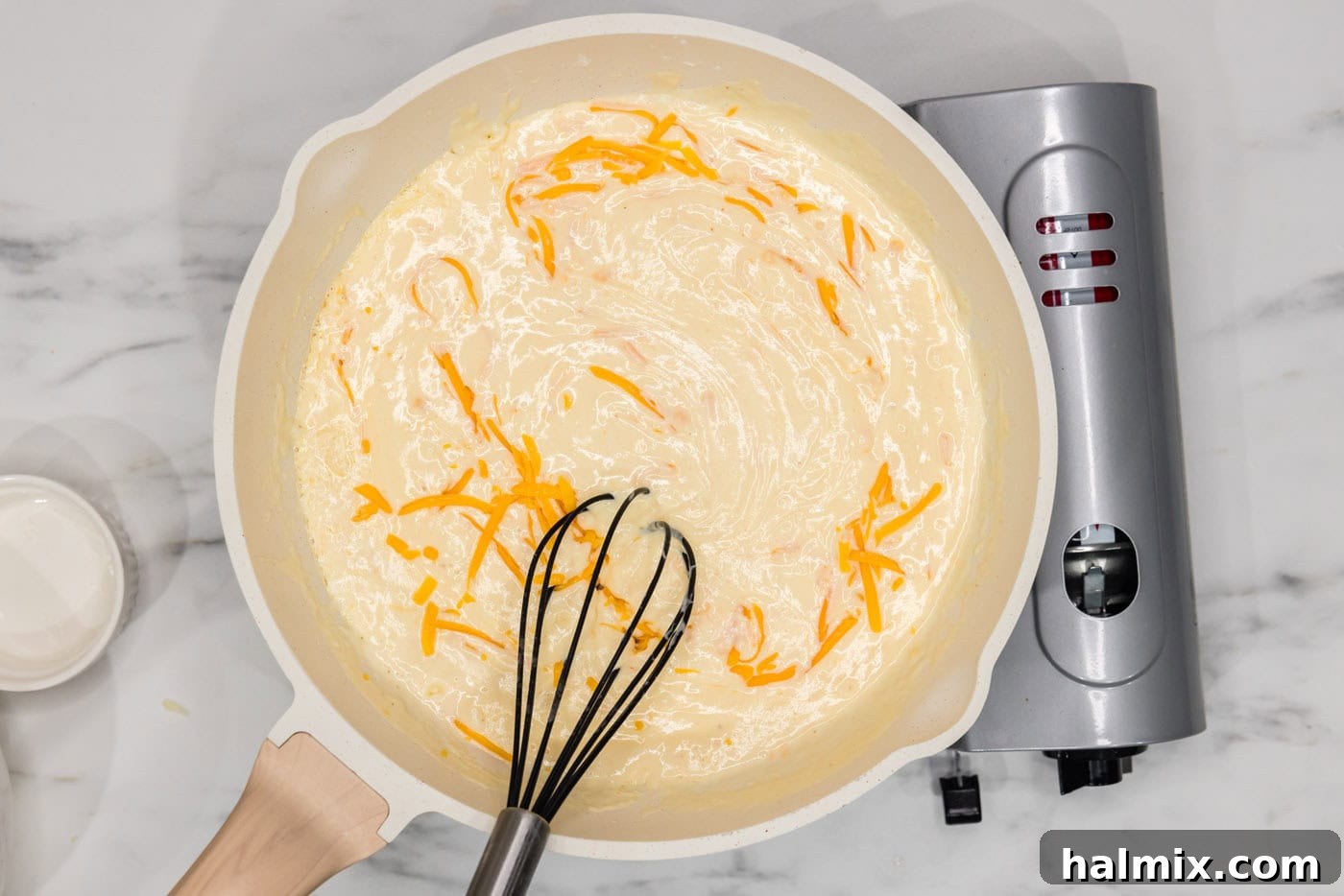 whisking shredded cheese into béchamel in a skillet