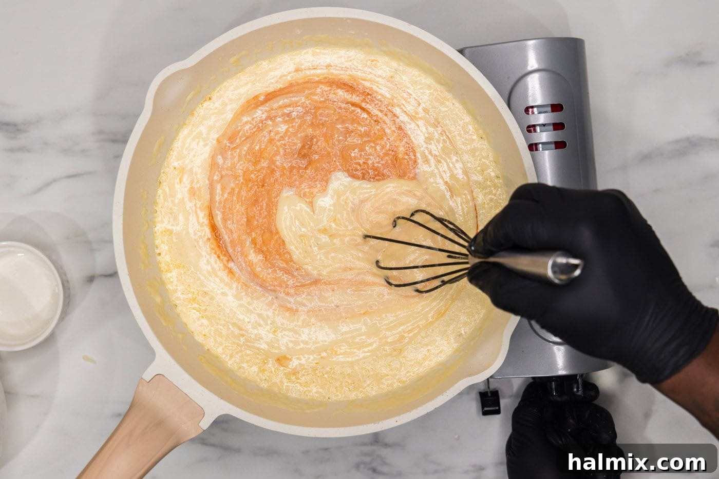 whisking hot sauce into mac and cheese sauce in a skillet