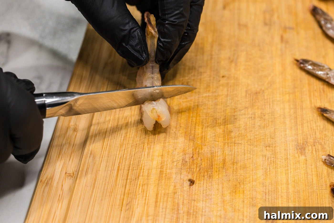 scoring shrimp with a knife on a cutting board, illustrating the technique to prevent curling