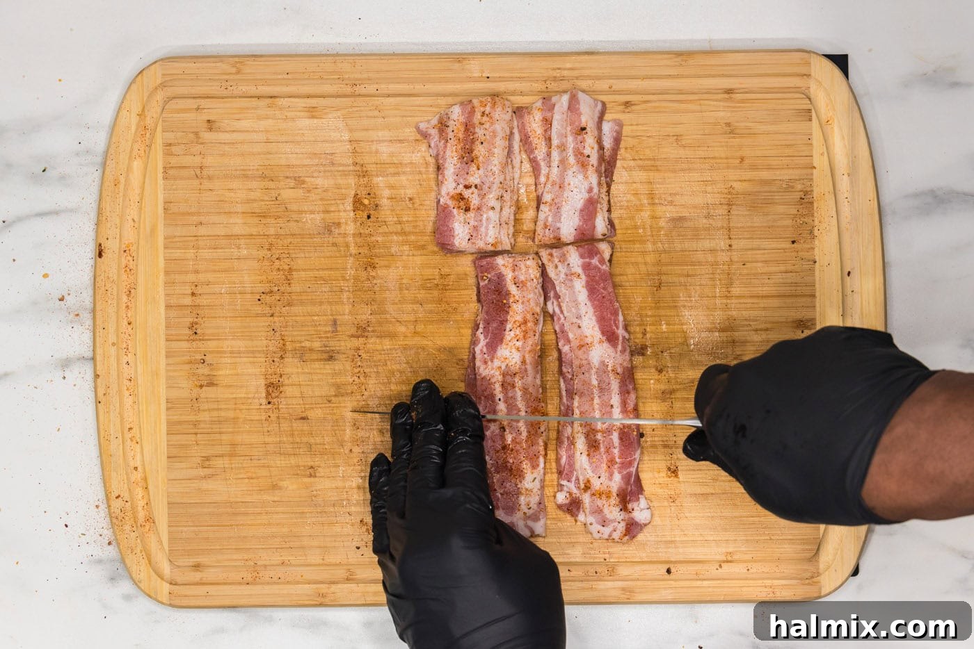 slicing bacon into thirds on a cutting board, showing preparation for wrapping