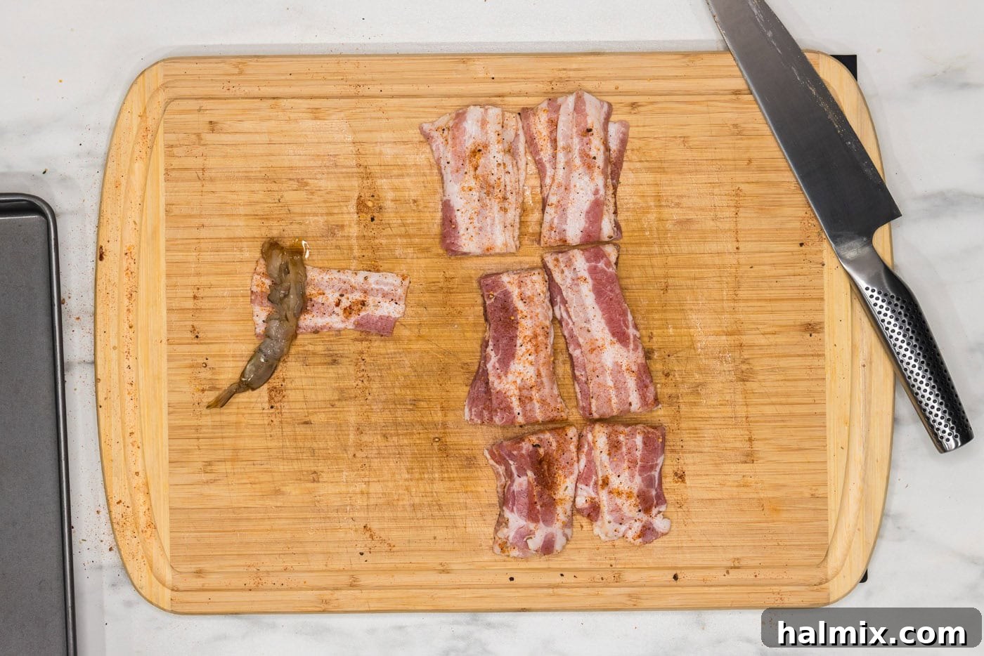 wrapping shrimp in bacon on a cutting board, demonstrating the technique