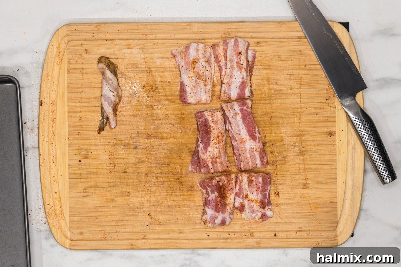 bacon wrapped shrimp next to bacon slices on a cutting board, ready for the air fryer
