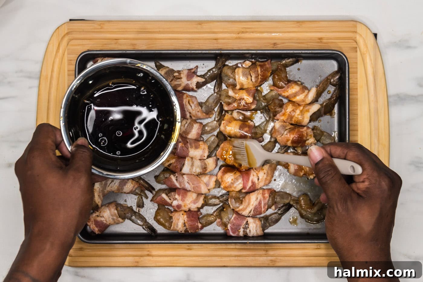 pouring soy sauce mixture over bacon wrapped shrimp on a baking sheet, showing the glazing process