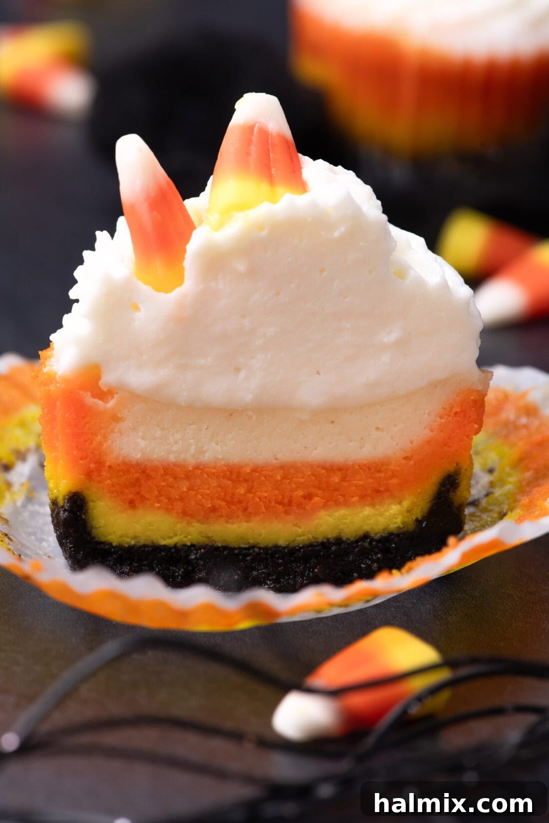 Spooky Sweet Candy Corn Cheesecake Minis 14 A mini Candy Corn Cheesecake cut in half, revealing the distinct yellow, orange, and white layers on an Oreo crust.