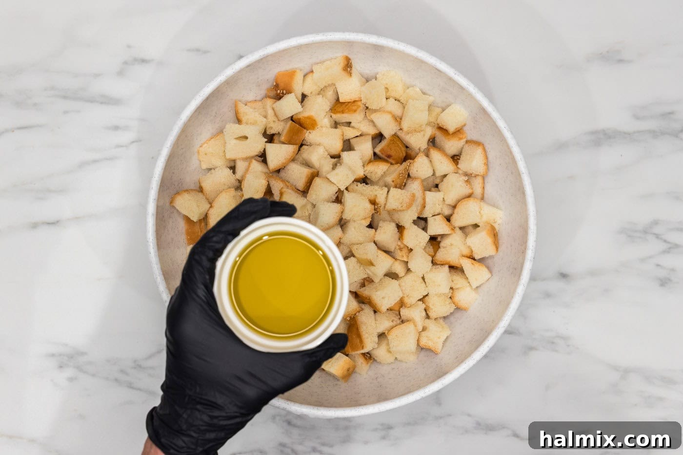 olive oil held over a bowl of cubed bread