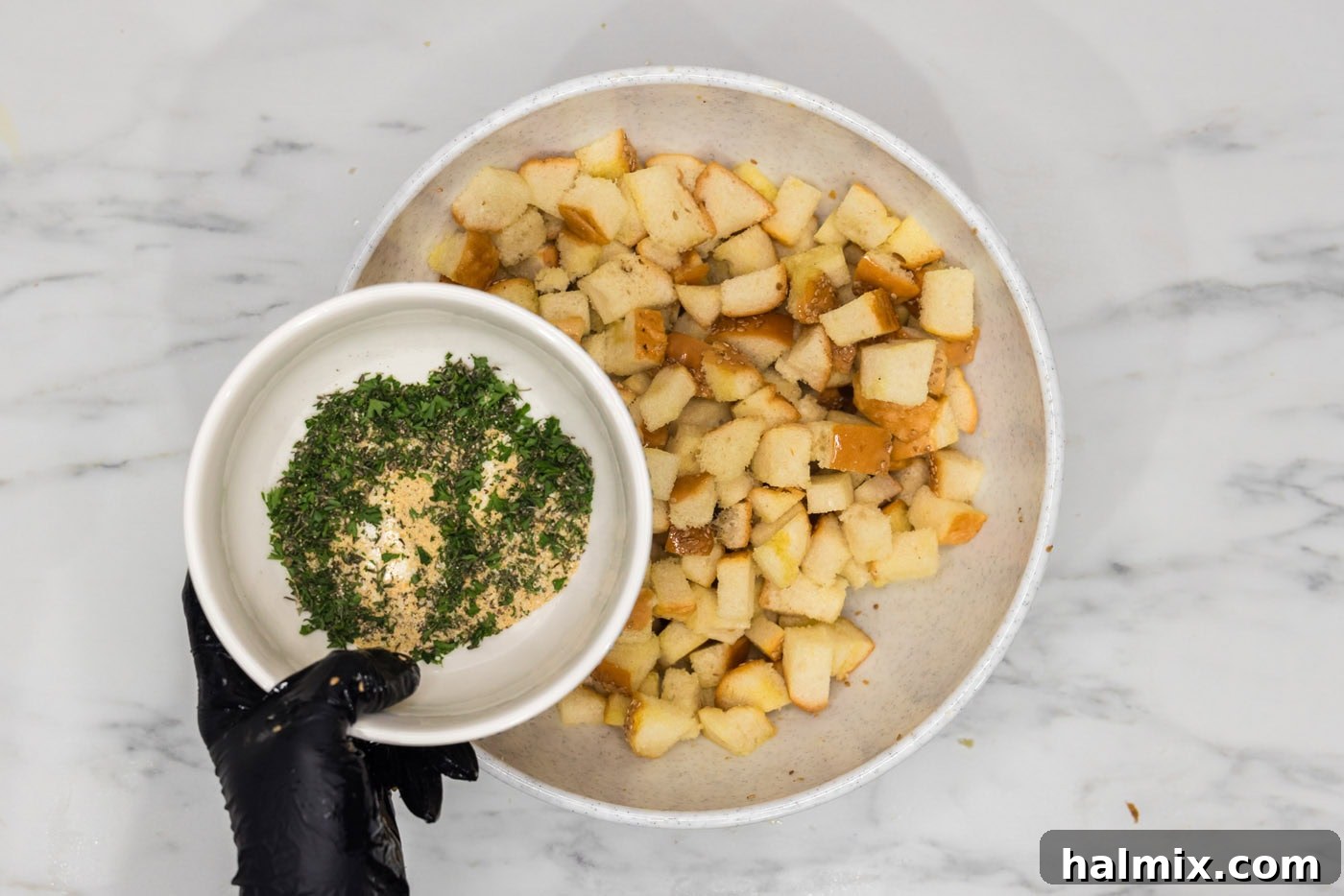 bowl of seasonings and herbs held over a bowl of cubed bread