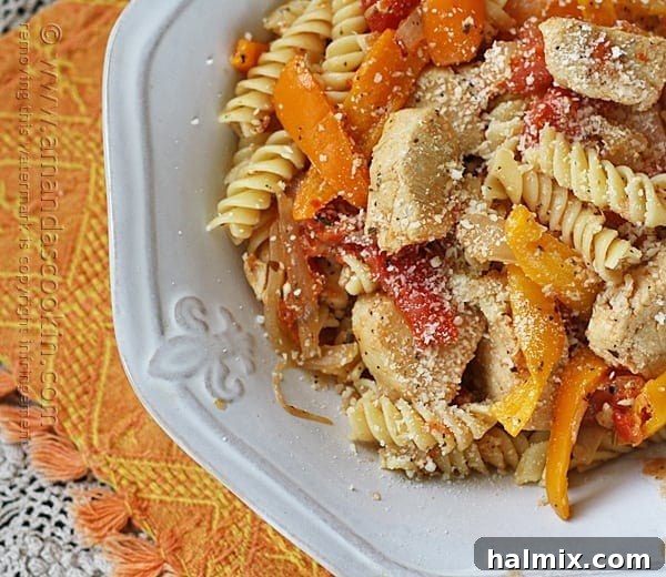 A close-up overhead photo of a vibrant Chicken with Peppers and Pasta dish in a white bowl, generously topped with freshly grated Parmesan cheese.