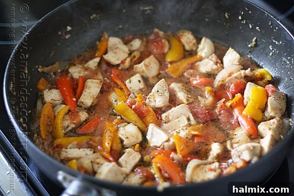 The skillet containing the chicken, peppers, tomatoes, and broth is brought to a boil and then simmered.