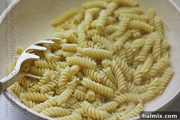 A close-up shot of a bowl of Rotini pasta being tossed to coat with Parmesan cheese.