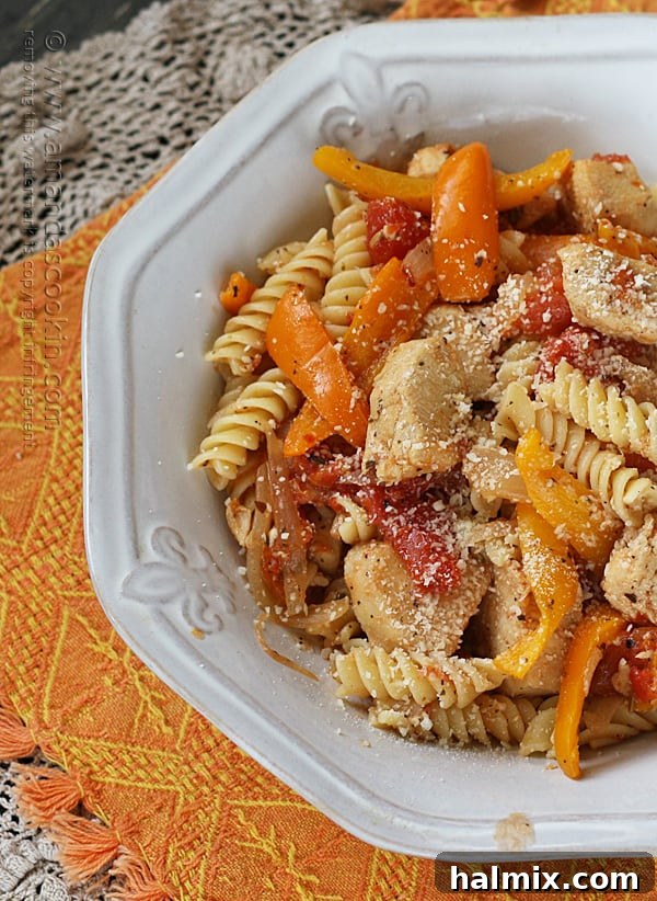 Another close-up overhead photo showcasing the appetizing texture of chicken with peppers and pasta in a white bowl, adorned with Parmesan cheese.