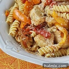 A close up photo of chicken with peppers and pasta in a white bowl topped with Parmesan cheese.