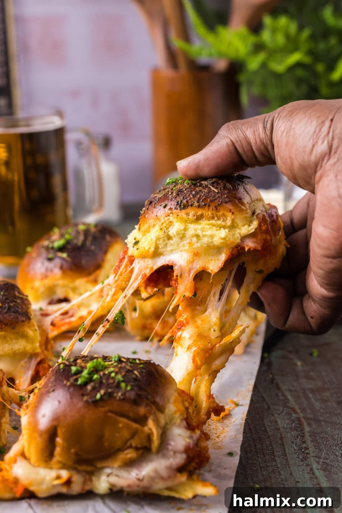 Hand pulling up a Chicken Parmesan Slider from a baking dish, showcasing melted cheese and crispy chicken