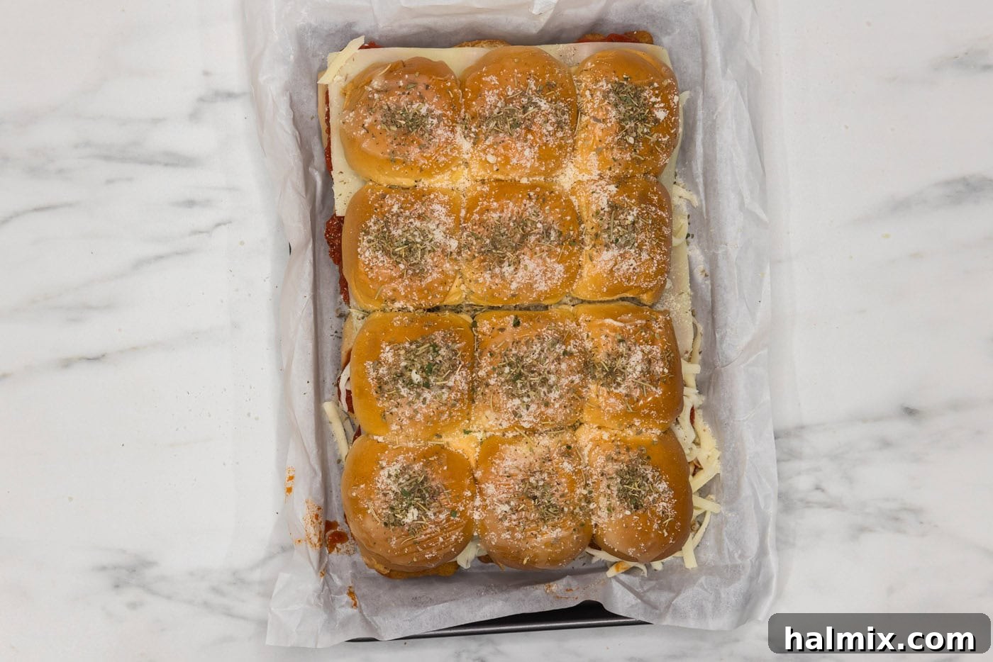 chicken parmesan sliders in a baking dish with parmesan cheese and italian seasoning