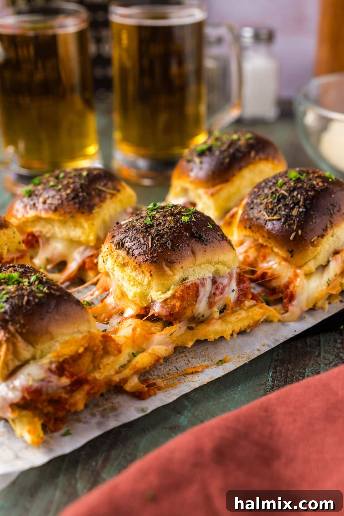 Close up photo of Chicken Parmesan Sliders arranged on parchment paper, showing the golden-brown buns and bubbly cheese