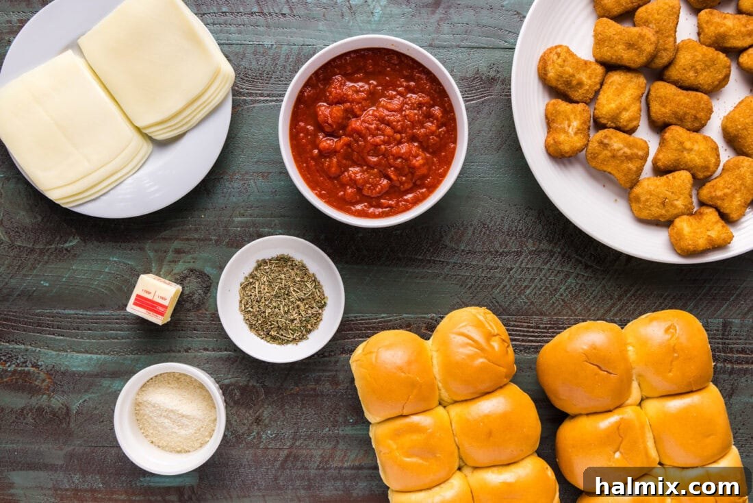 Ingredients for Chicken Parmesan Sliders laid out on a table, including buns, chicken nuggets, marinara, and cheeses