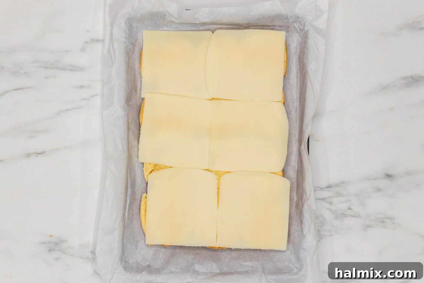 sliced mozzarella on top of slider buns in a baking dish