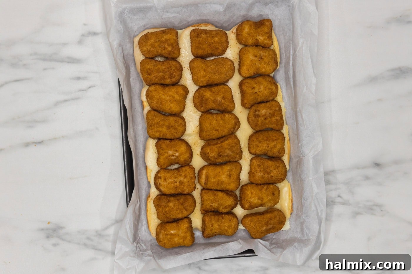 chicken nuggets on top of sliders buns and cheese in a casserole dish