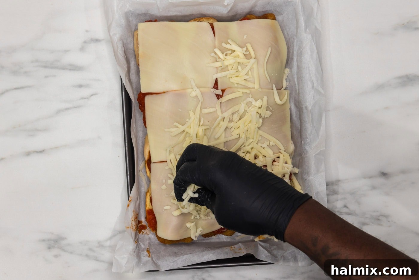 sprinkling shredded mozzarella cheese over sliders