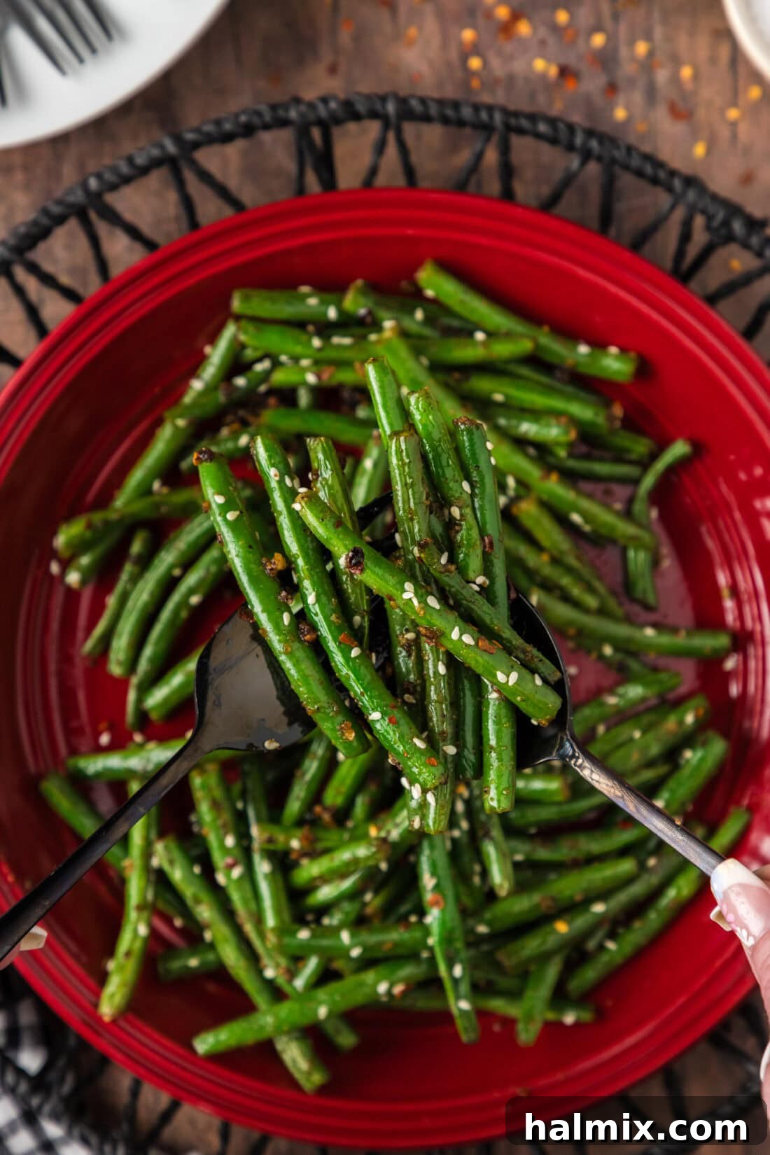 Sautéed Green Beans with Garlic and Lemon Zest 3 Serving utensils holding up Sautéed Green Beans above a plate, showcasing their perfect texture and vibrant green color.