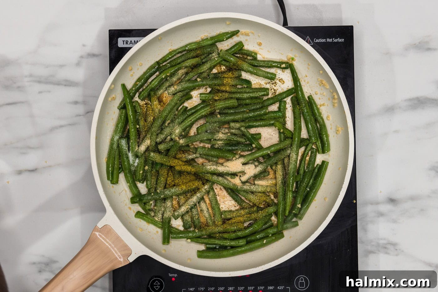 Sautéed Green Beans with Garlic and Lemon Zest 6 Green beans in a skillet being seasoned with a blend of sesame oil, salt, onion powder, and lemon pepper.