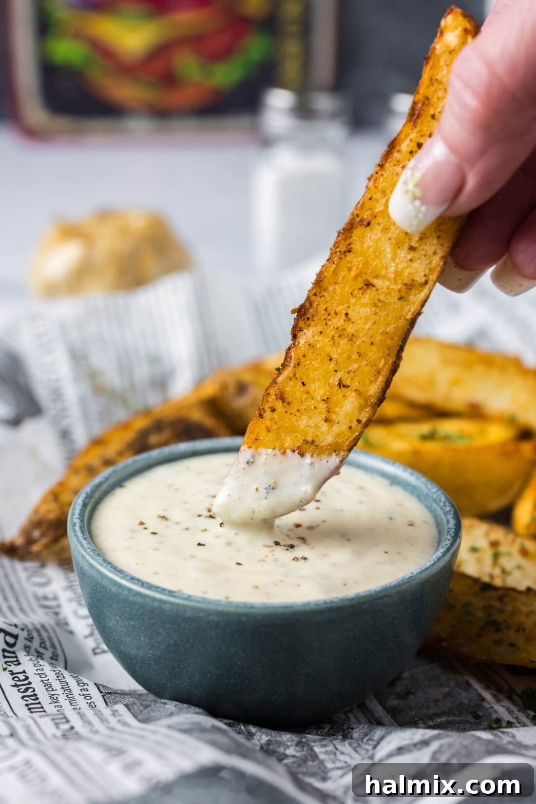 A crispy potato wedge being dipped into a bowl of rich, creamy homemade Garlic Aioli, highlighting its perfect dipping consistency.