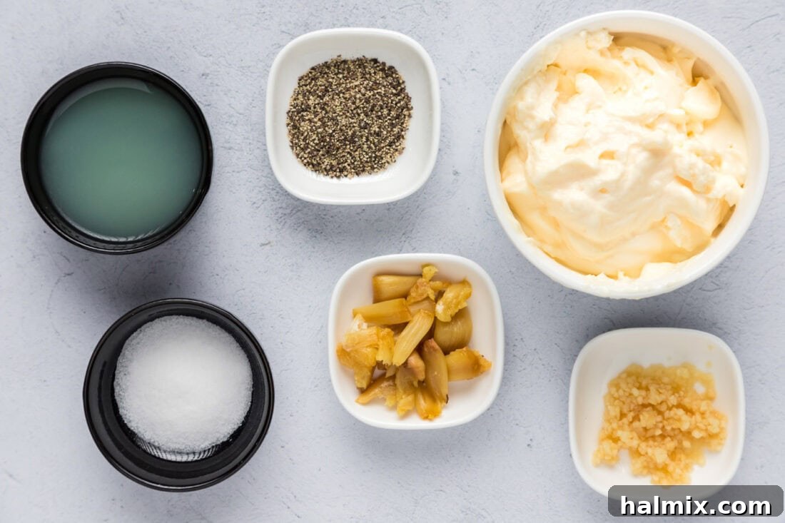 All the fresh ingredients for making homemade Garlic Aioli laid out on a clean surface, including mayonnaise, a head of roasted garlic, fresh lemon, and spices.