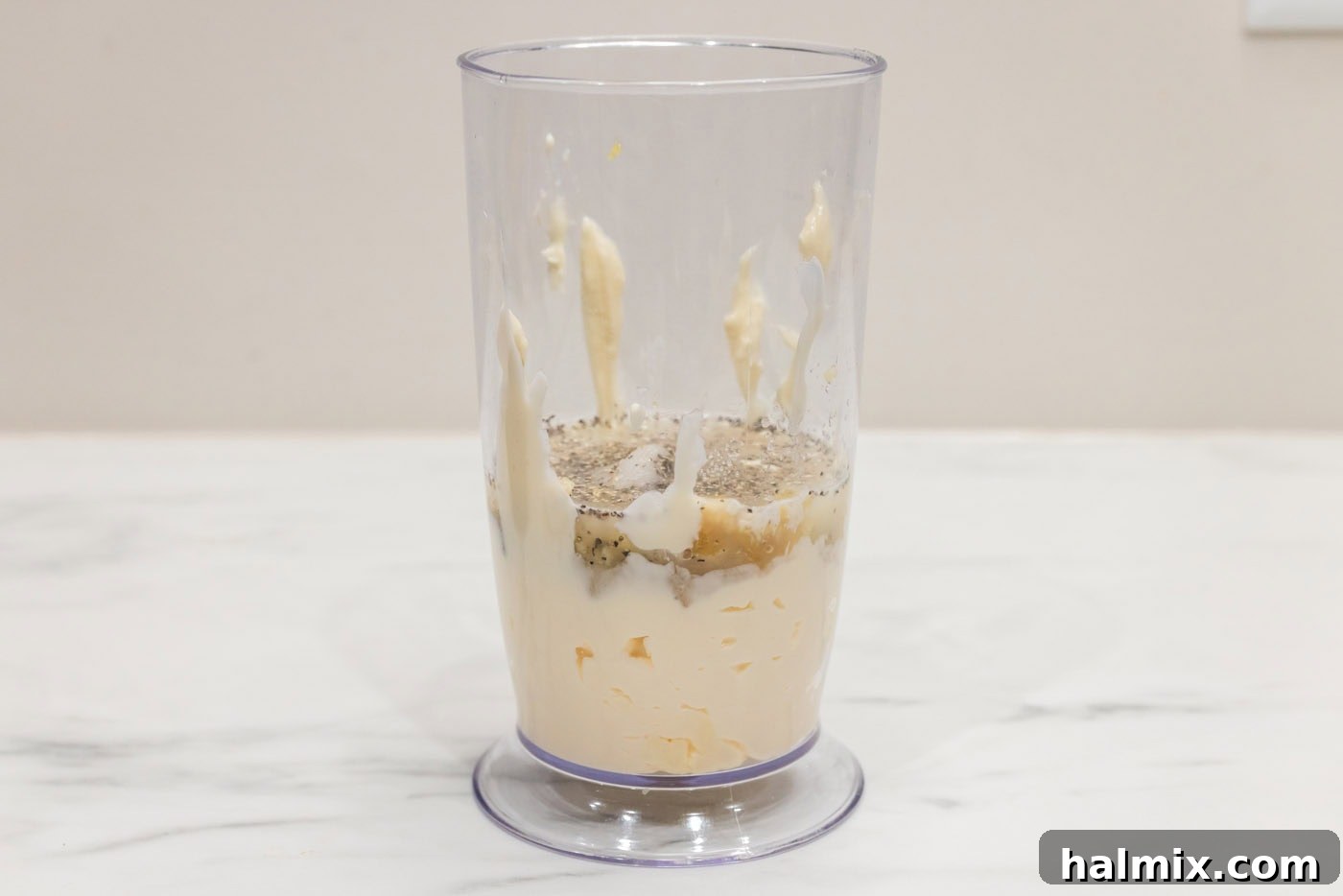 All the ingredients for Garlic Aioli, including mayonnaise, roasted garlic, minced garlic, lemon juice, salt, and pepper, are placed in a container ready for immersion blending.